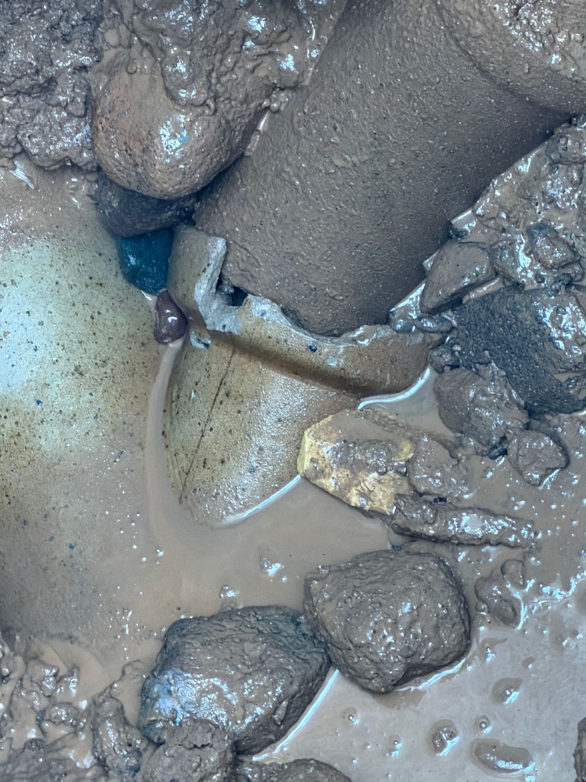 Broken pipe surrounded by mud and rocks, showing a split in the pipe and dark mud around it.