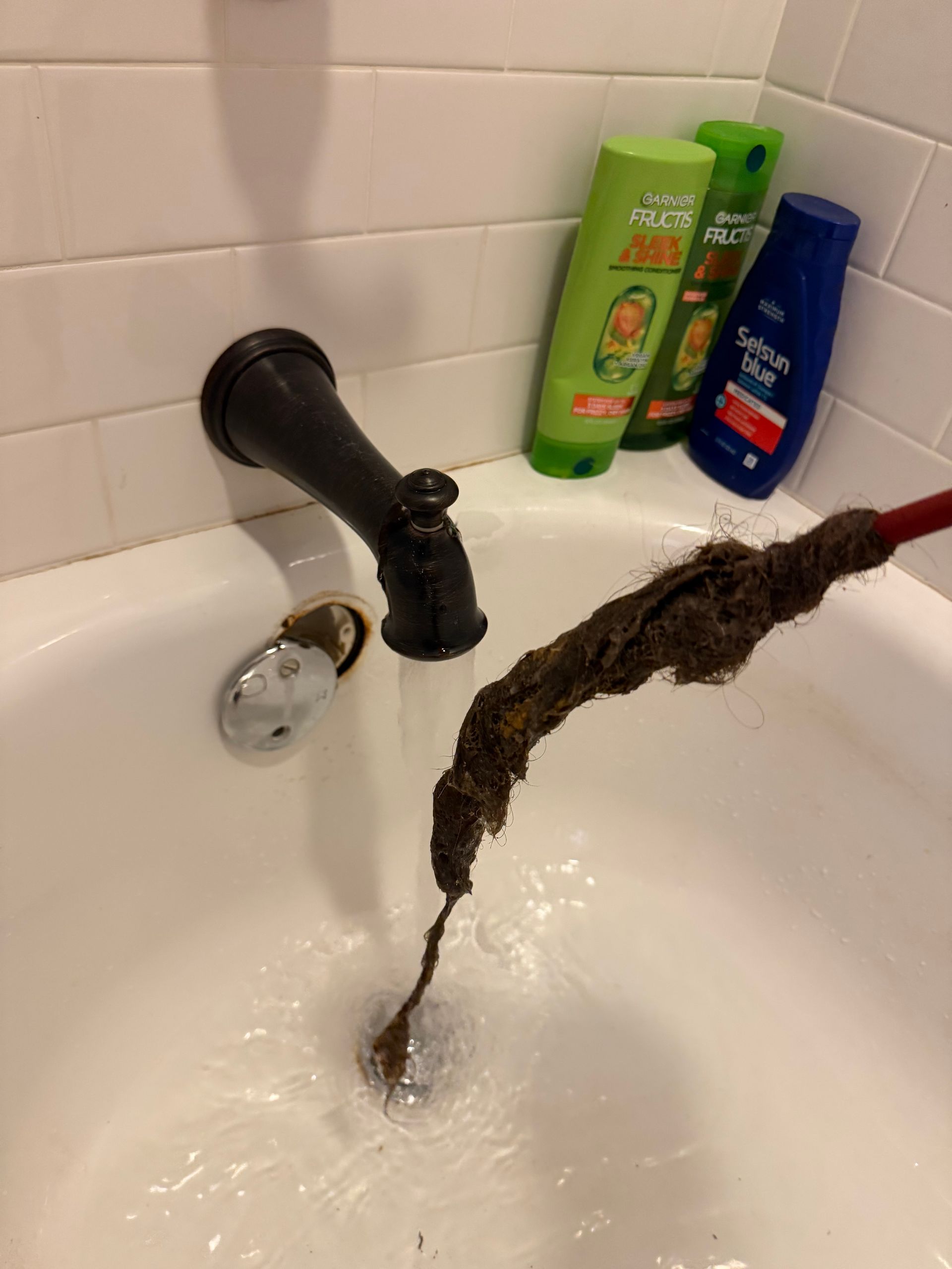 A person wearing yellow gloves is cleaning a drain with a hose.