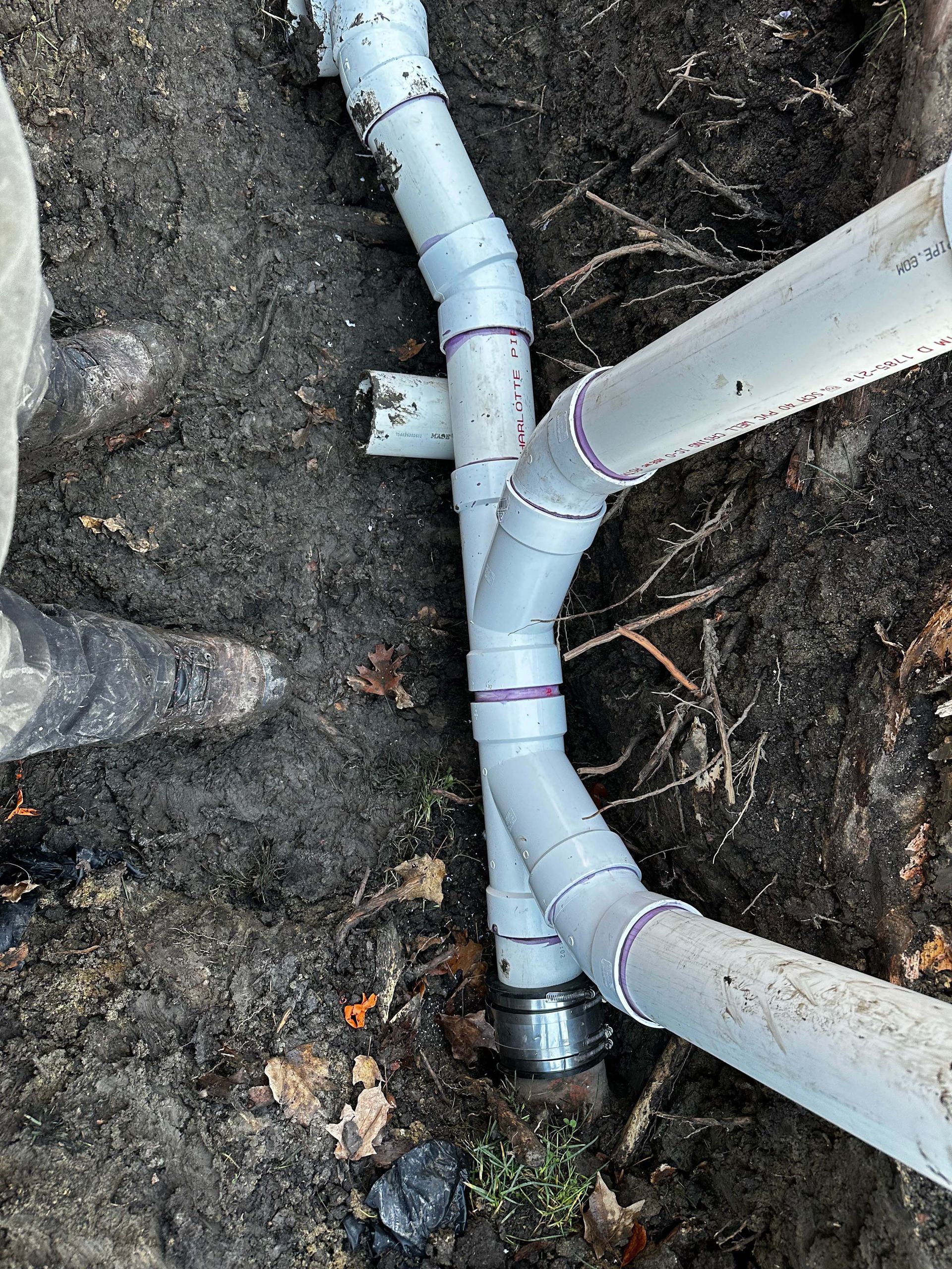Grey PVC pipes being installed in a dirt trench outdoors.