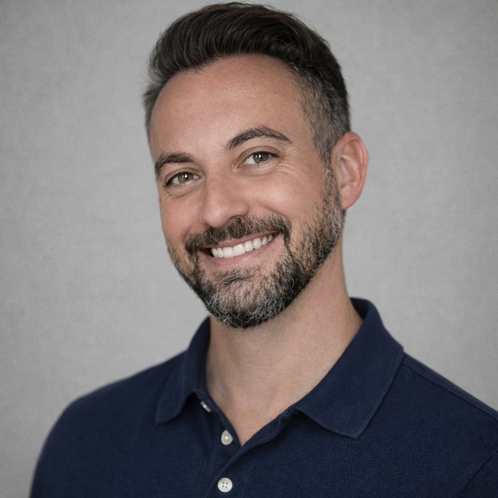Man with dark hair and beard smiles, wearing a navy blue polo shirt.