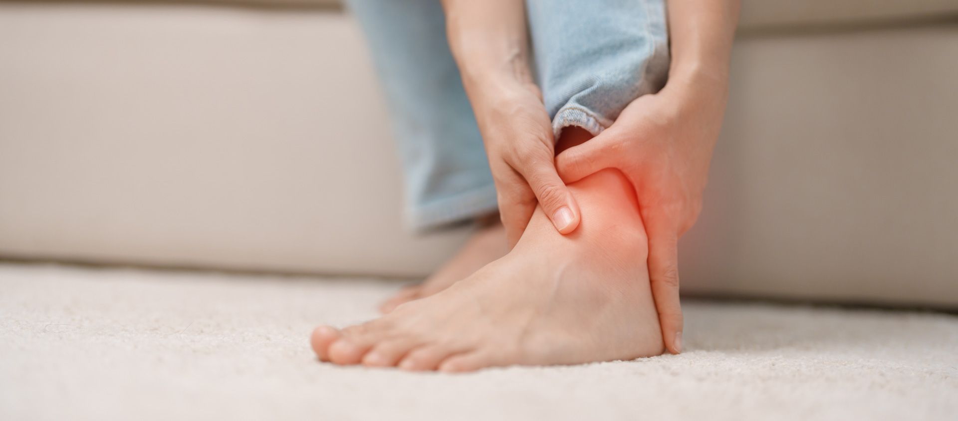 A woman is holding her ankle in pain while sitting on a couch.
