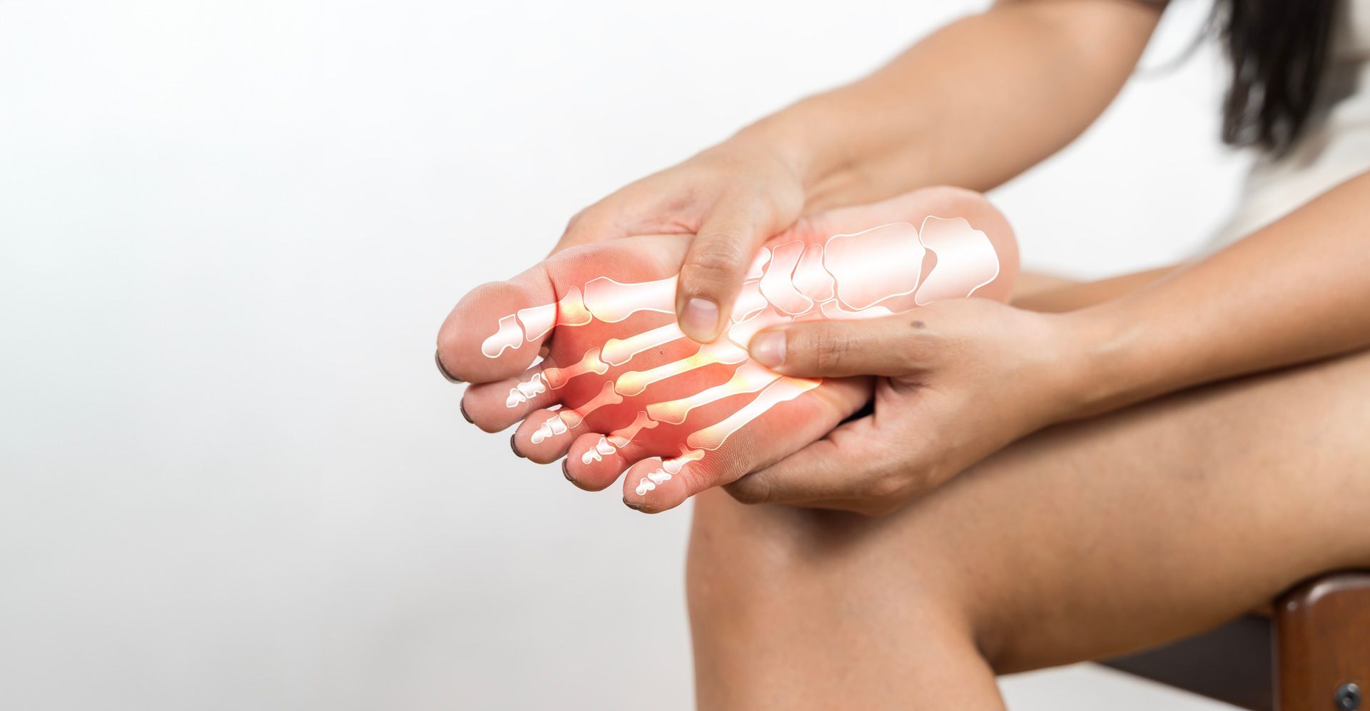 A woman is sitting on a chair holding her foot in pain.