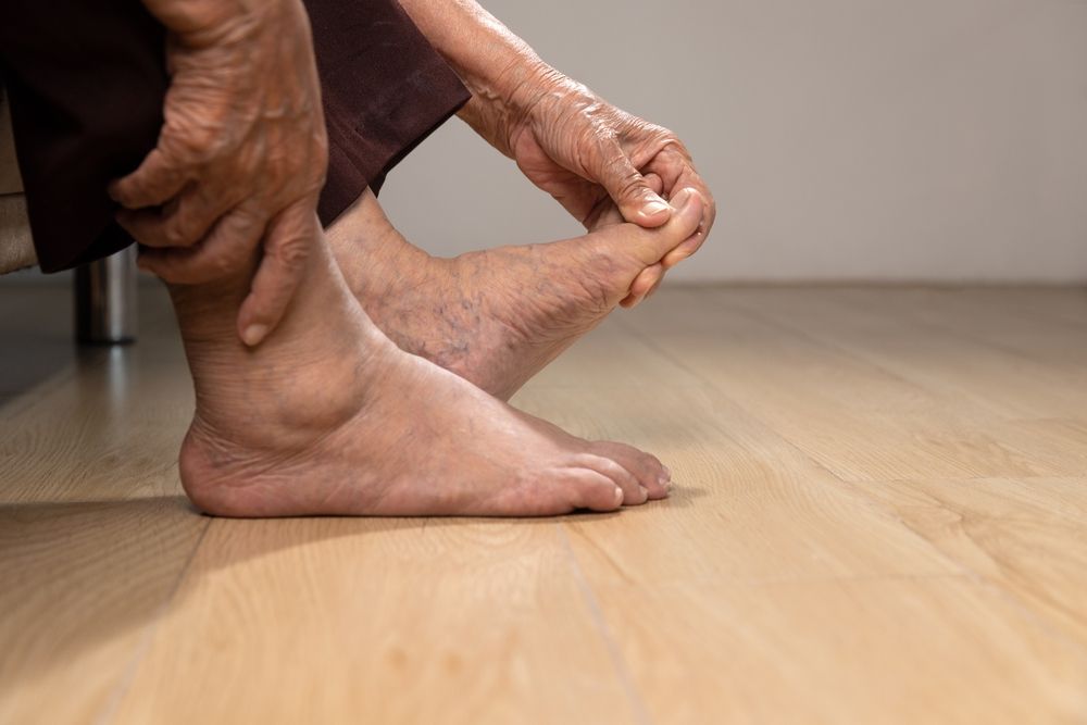 A person is holding their foot in pain on a wooden floor.