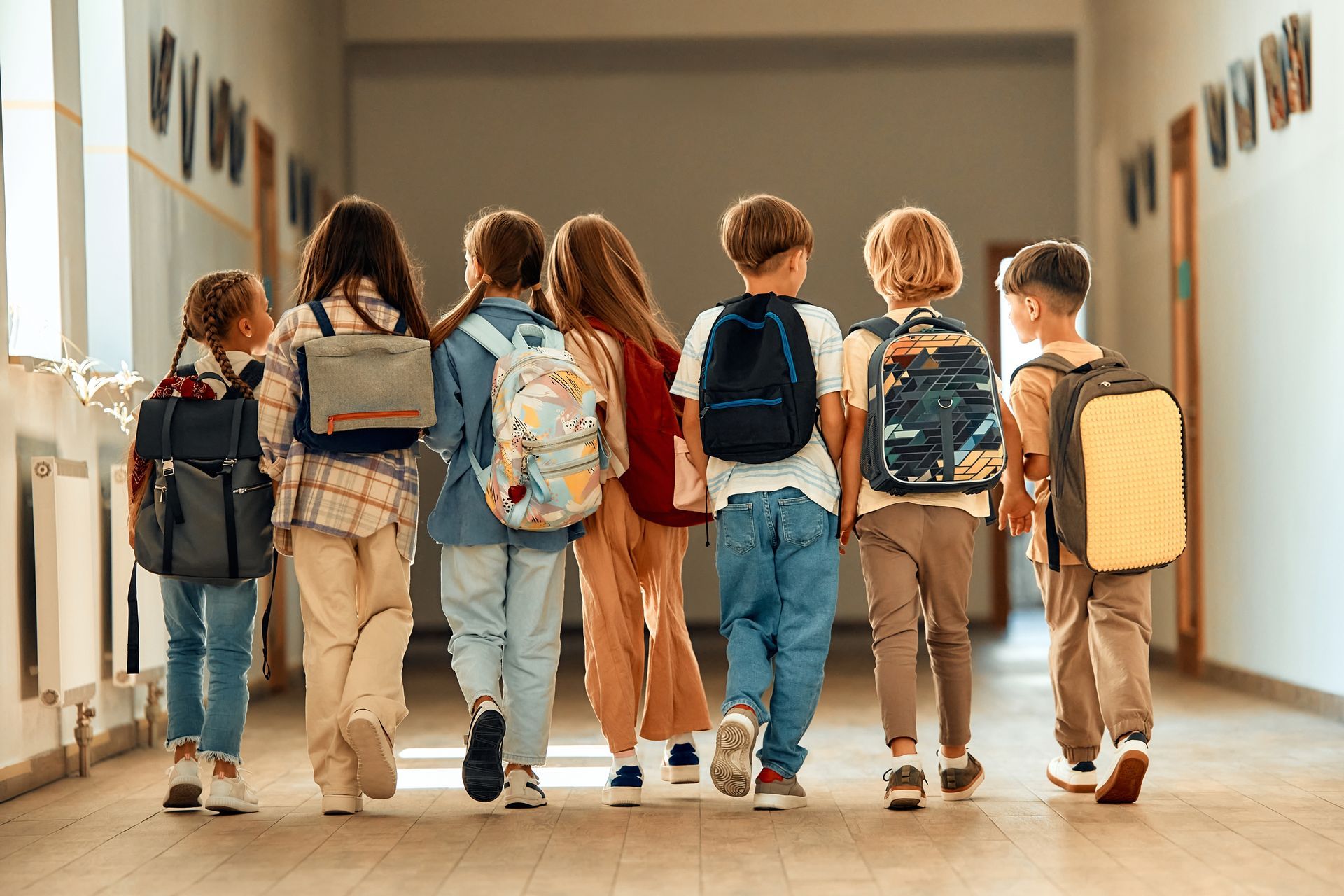 A group of children with backpacks are walking down a school hallway.