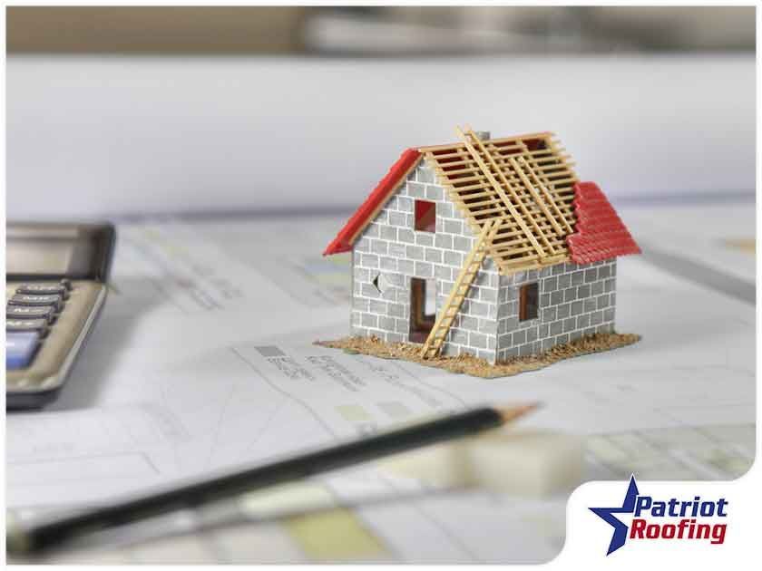 A small model house is sitting on top of a table next to a calculator and pencil.