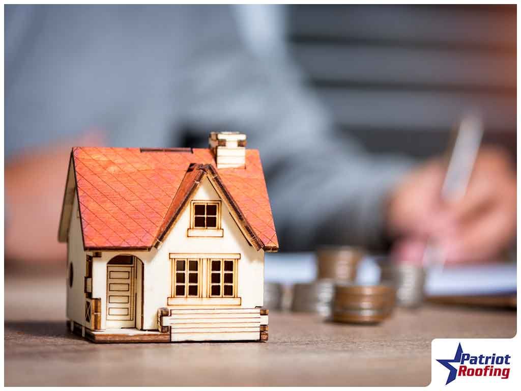 A small wooden house is sitting on a table next to a pile of coins.