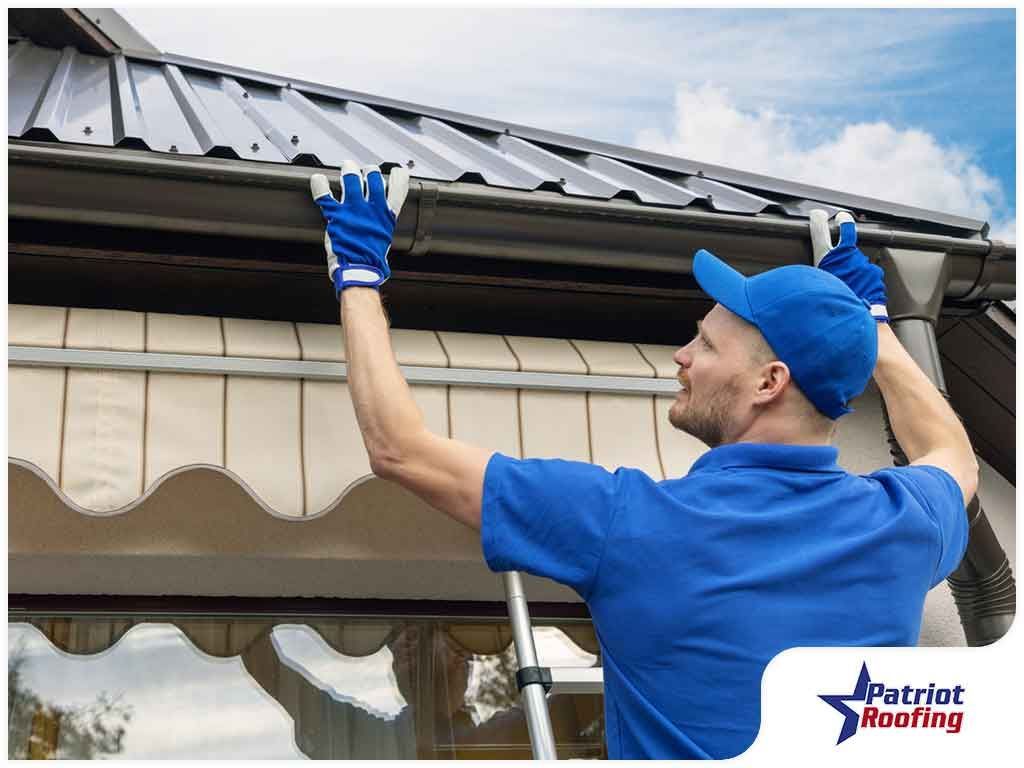 A man is standing on a ladder fixing a gutter on a roof.