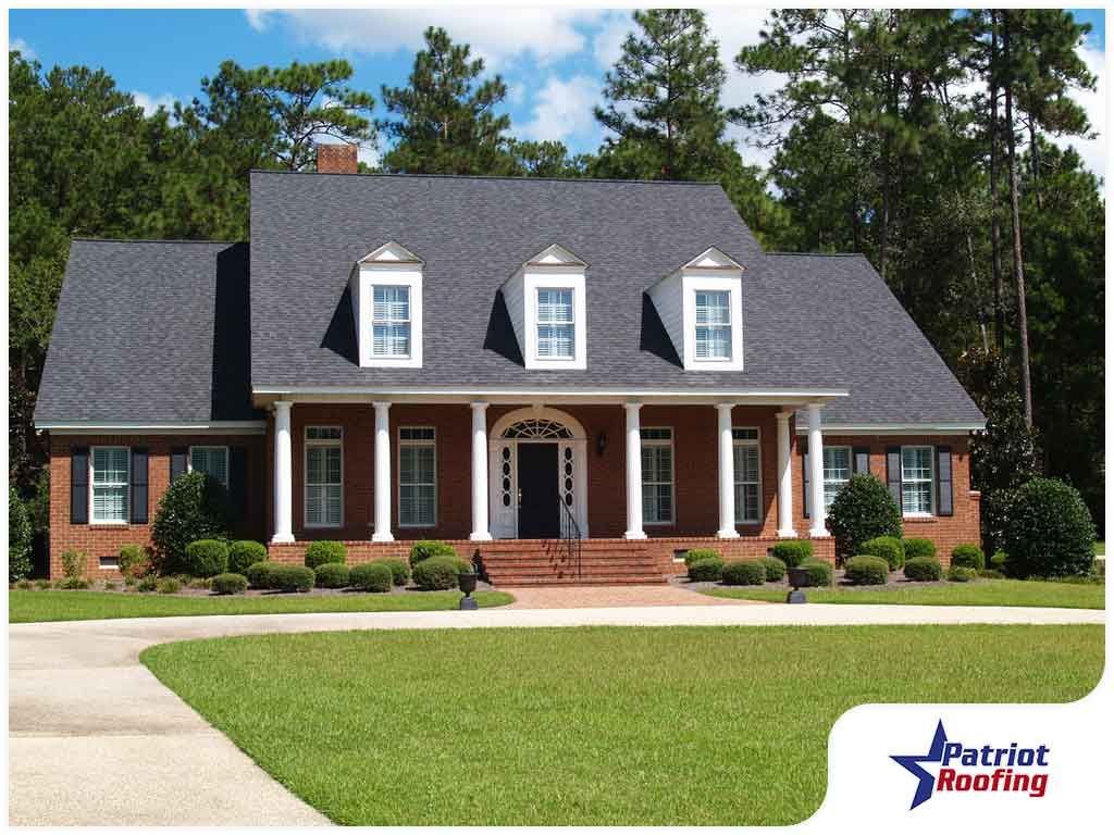 A large brick house with a patriot roofing logo in the corner
