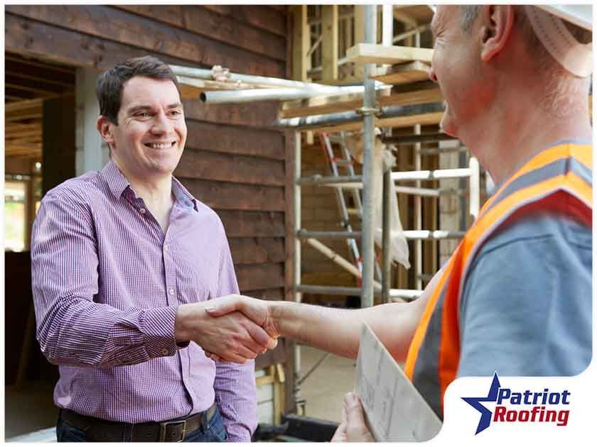 A man is shaking hands with a construction worker in front of a building under construction.