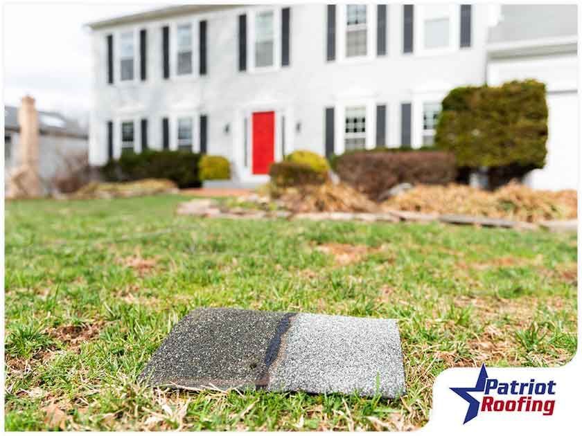 A piece of shingles is laying on the grass in front of a house.