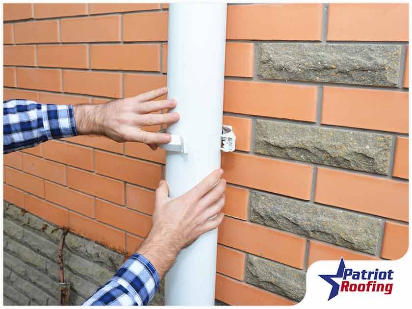 A man is fixing a gutter on a brick wall.