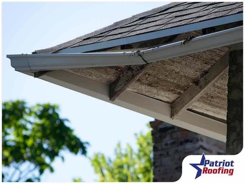 A close up of a gutter on a roof with a patriot roofing logo in the corner.