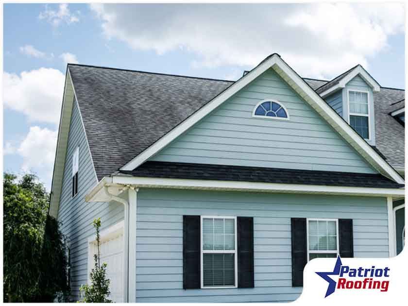 A blue house with black shutters and a patriot roofing logo
