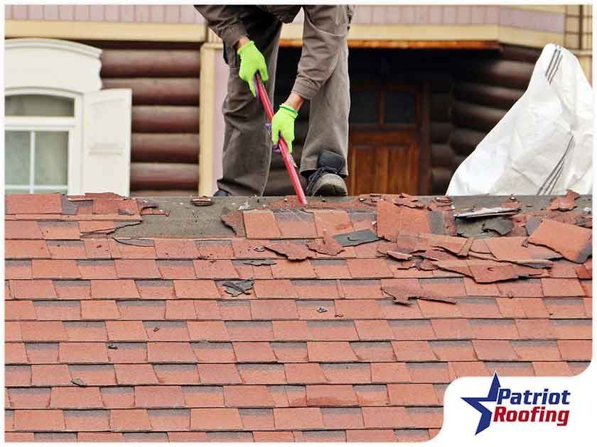 A man is standing on top of a roof with a hammer.