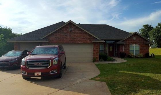 Two cars are parked in front of a brick house.