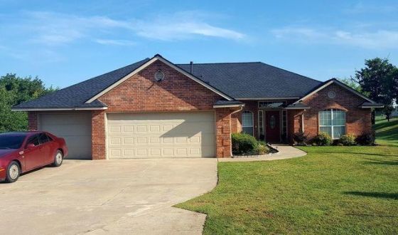A red car is parked in front of a brick house.