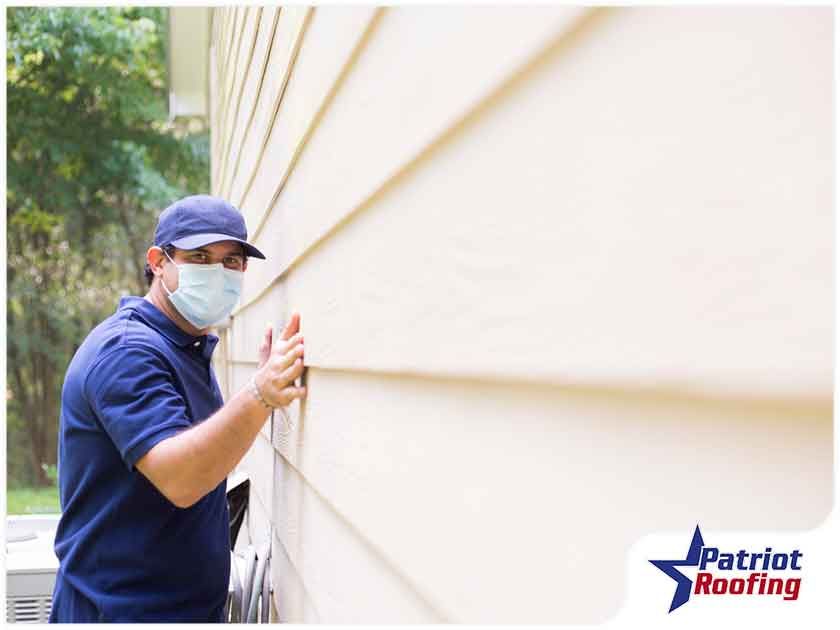 A man wearing a mask is working on the side of a house.