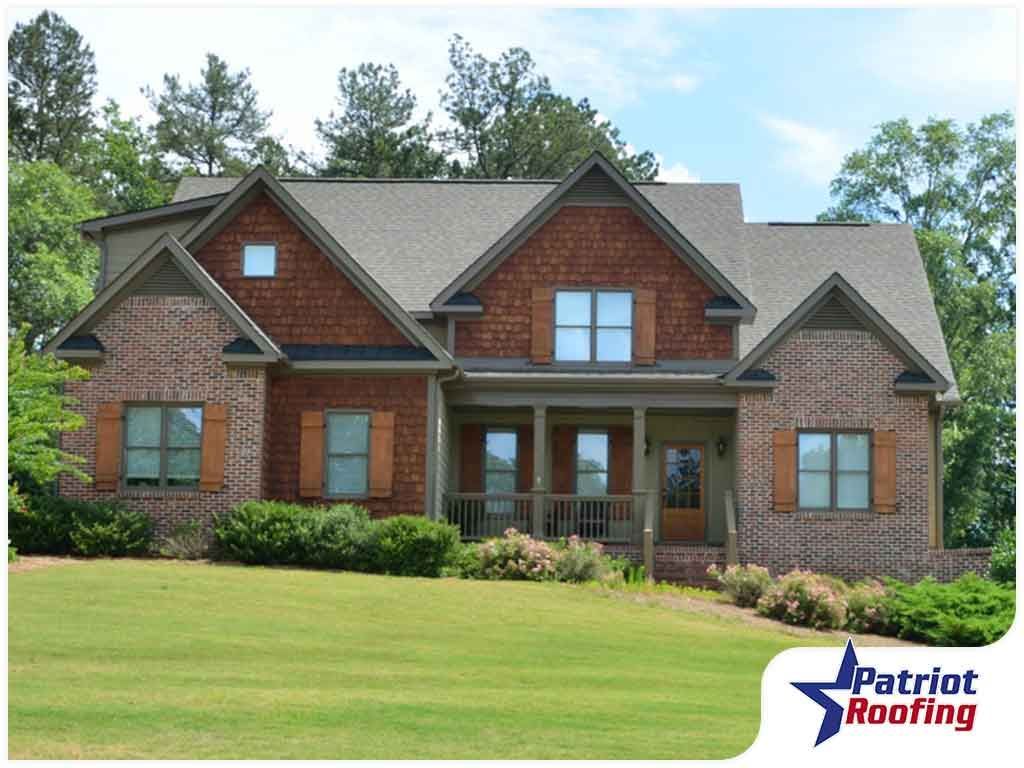 A large brick house with a patriot roofing logo in the corner