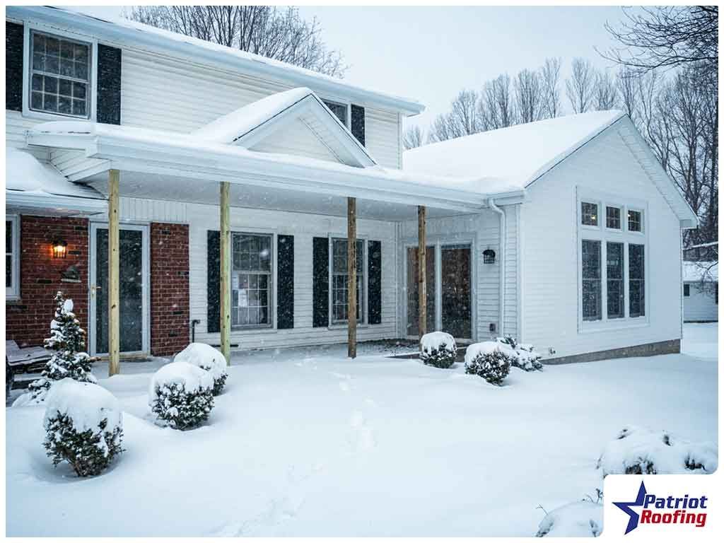 A white house with black shutters is covered in snow.