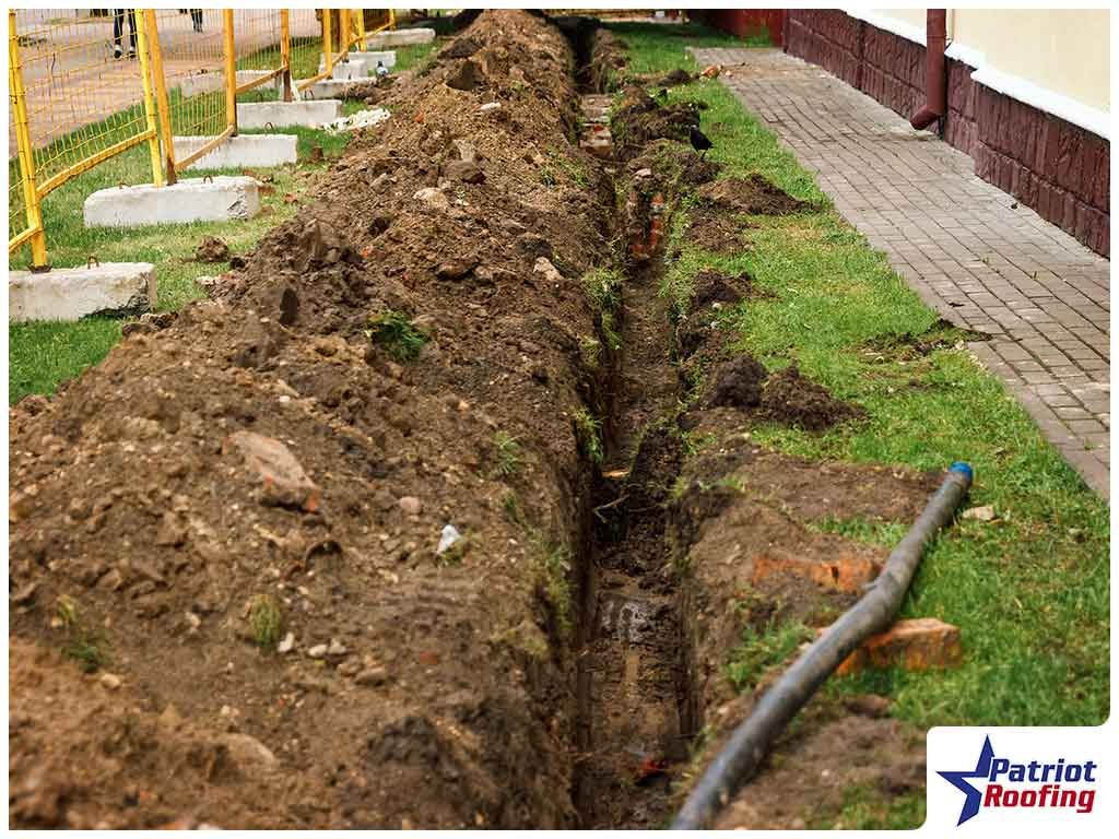 A trench is being dug in the grass in front of a building.