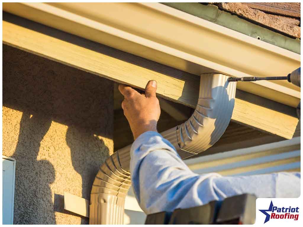 A man is fixing a gutter on a house with a screwdriver.