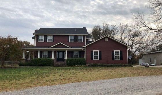 A large red house with a black roof is sitting in the middle of a grassy field.
