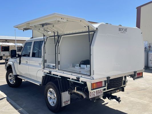 A white truck with a canopy on top of it is parked in a parking lot.
