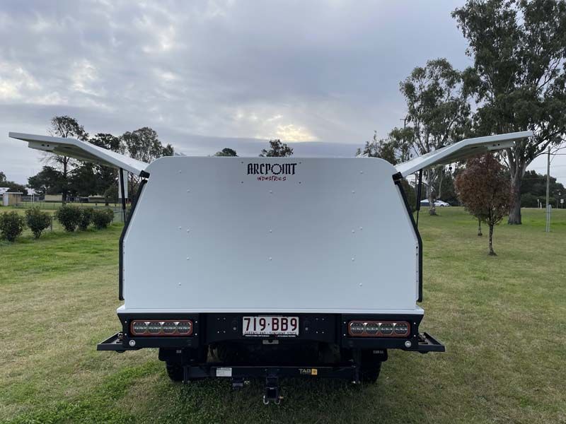 A white truck with a canopy is parked in a grassy field.