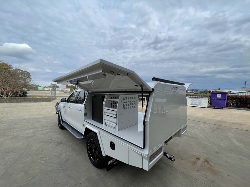 A white truck with a canopy on top of it is parked in a parking lot.