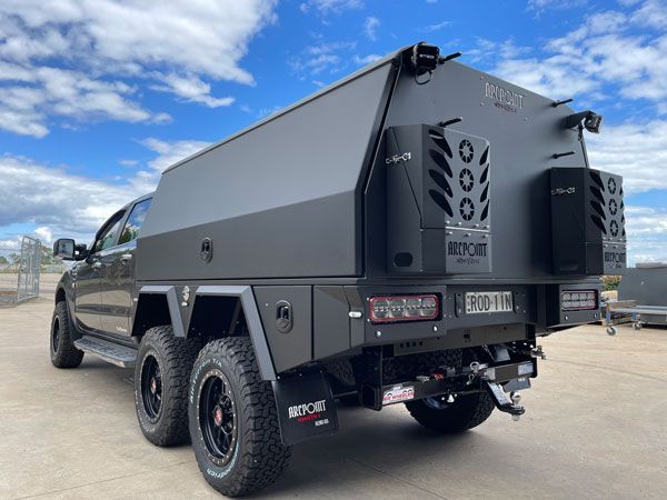 A black truck with a canopy on top of it is parked on the side of the road.