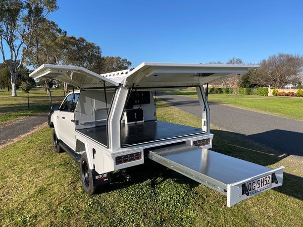 A white truck with a canopy open is parked in a grassy field.