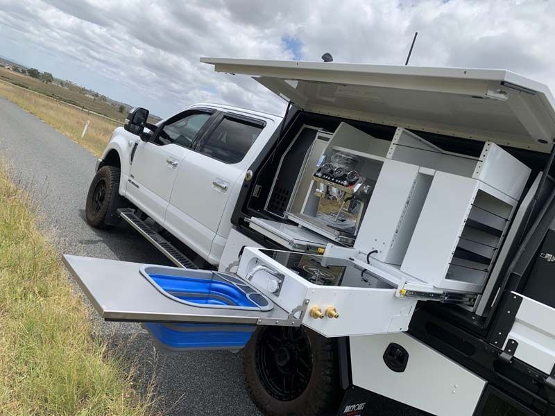 A white truck with a sink in the back is parked on the side of the road.