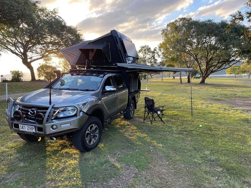A truck with a tent on top of it is parked in a grassy field.