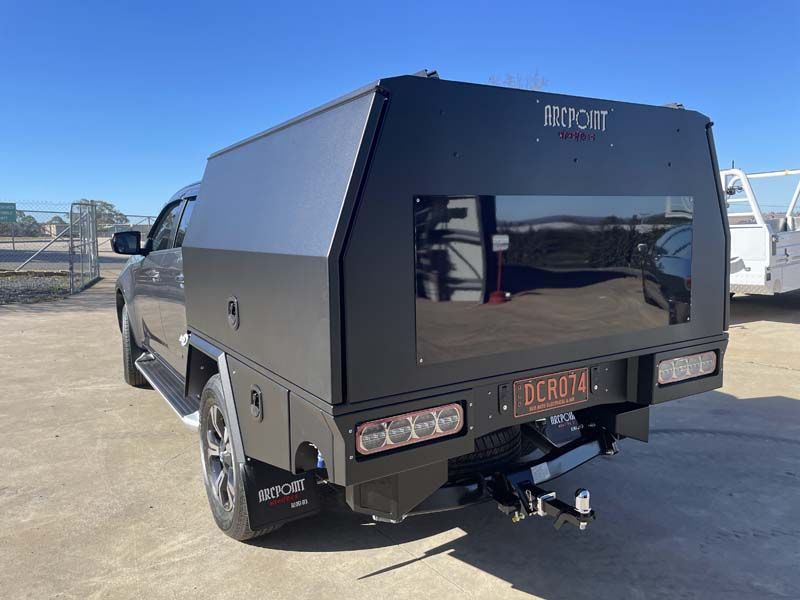 A black truck with a canopy is parked in a parking lot.