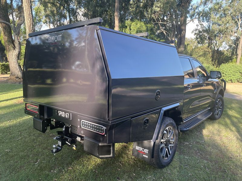 A black truck with a canopy is parked in a grassy field.