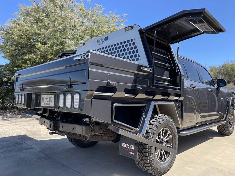 A black truck with a tray and canopy is parked in a parking lot.