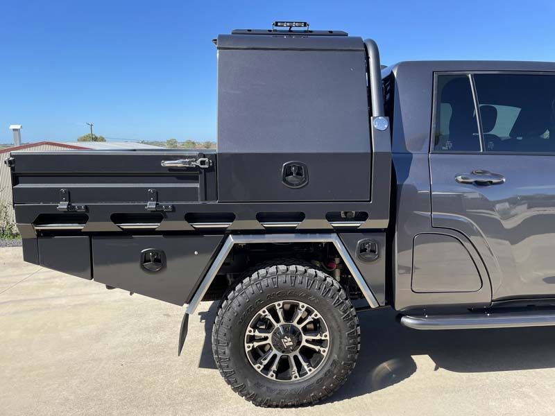 A gray truck with a tray on the back is parked on the side of the road.