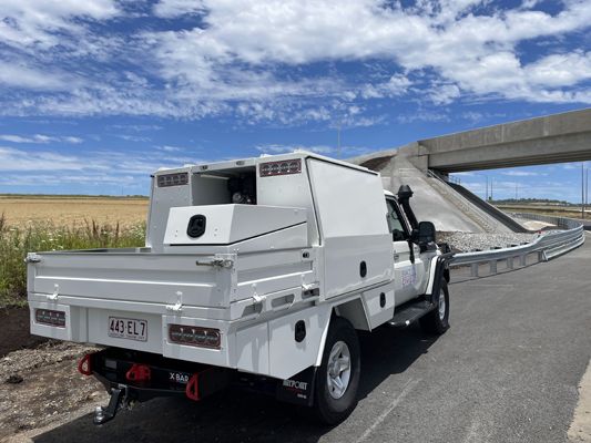 A white truck is parked on the side of the road next to a bridge.