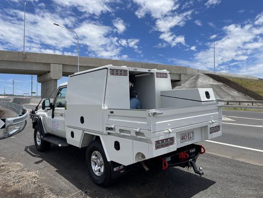 A white truck is parked on the side of the road next to a bridge.