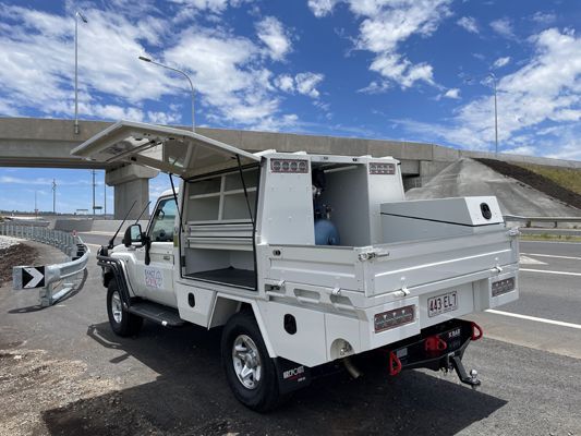 A white truck is parked on the side of the road next to a bridge.