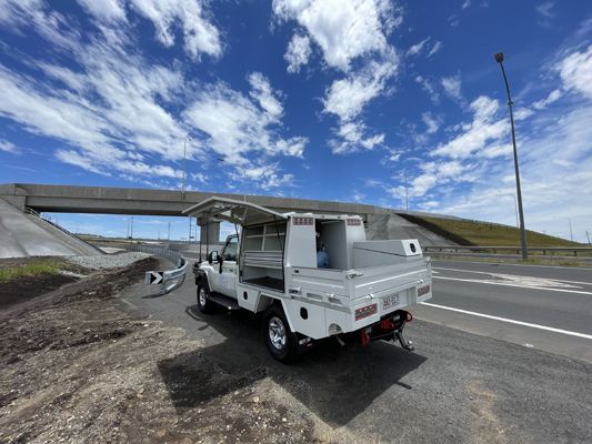 A white truck is parked on the side of the road under a bridge.