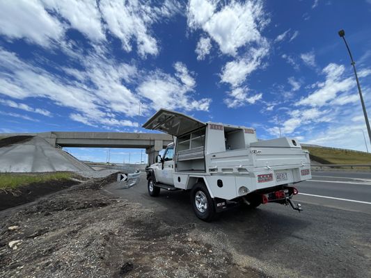 A white truck is parked on the side of the road next to a bridge.