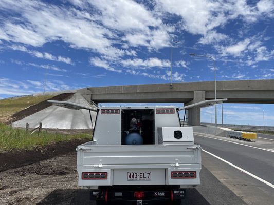 A white truck is parked on the side of a highway next to a bridge.