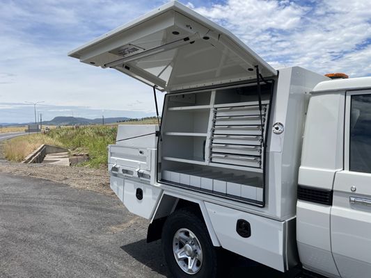 A white truck with the canopy open is parked on the side of the road.