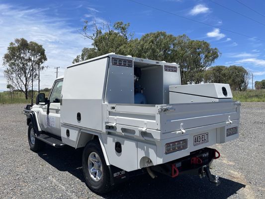 A white truck with a utility bed is parked in a gravel lot.