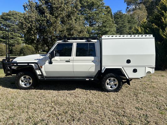 A white truck with a canopy is parked in a grassy field.