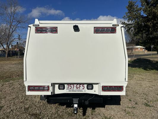 The back of a white truck is parked in a grassy field.