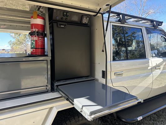A white truck with a refrigerator and a fire extinguisher in the back.