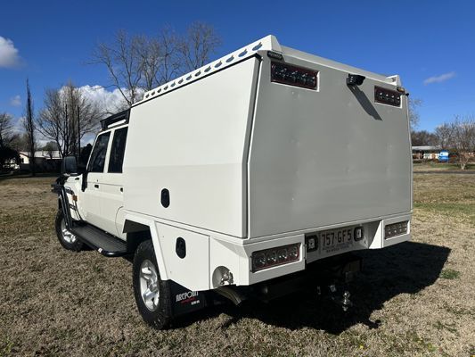 A white truck with a canopy on top of it is parked in a field.