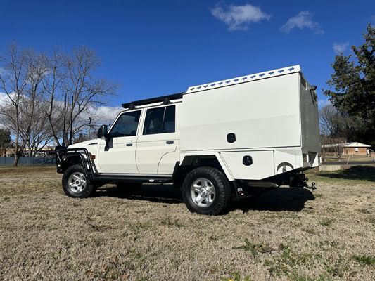 A white truck with a canopy on top of it is parked in a field.